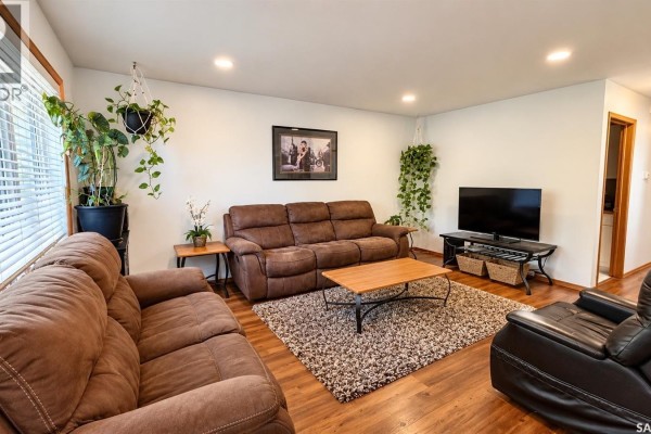 Living room with two brown reclining sofas, a coffee table, and a television on a stand. - 717 31st Street W, Saskatoon