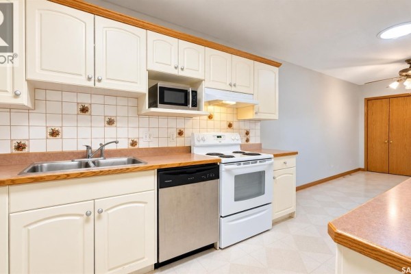 Kitchen with cream cabinets, a white stove, a stainless steel dishwasher, and a double sink. - 717 31st Street W, Saskatoon