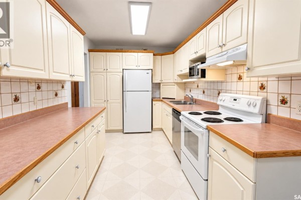 Long kitchen with cream cabinets, white appliances including a refrigerator, and light pink countertops. - 717 31st Street W, Saskatoon