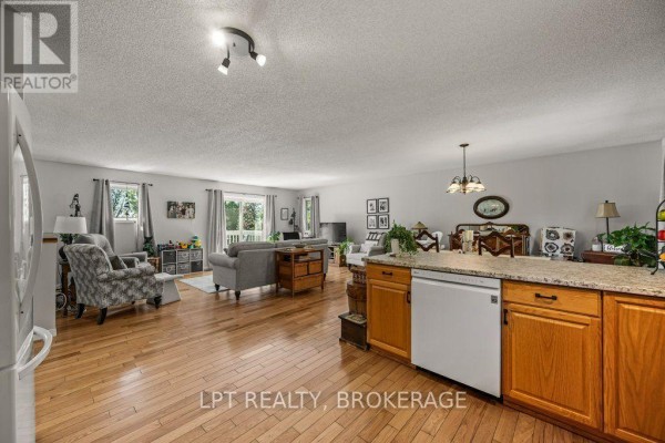 Front exterior view of a large brick house with a white deck, covered porch, and manicured lawn. - 717 County 14 Road, Stone Mills