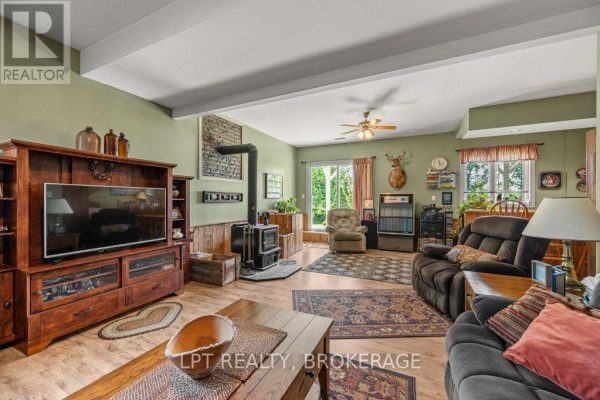 Covered patio area with seating, rocking chair, and plants, adjacent to a brick exterior wall and white door. - 717 County 14 Road, Stone Mills