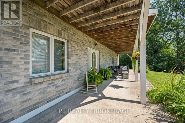 Rear exterior view of a light-colored home with a two-car garage, wooden deck, and green grass. - 717 County 14 Road, Stone Mills