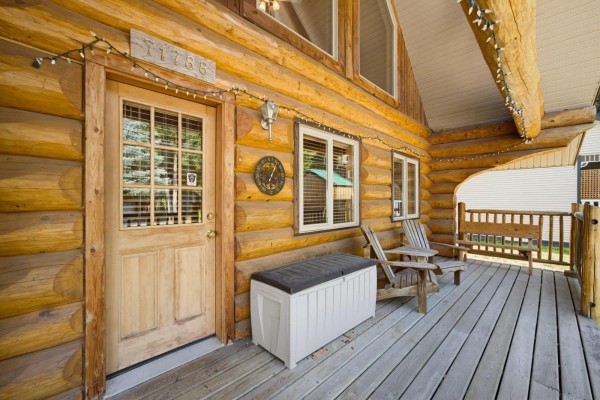 Close-up of the log cabin's front door, wooden porch, and windows with Adirondack chairs. - 71788 Meadow Road, Sunshine Valley, Sunshine Valley
