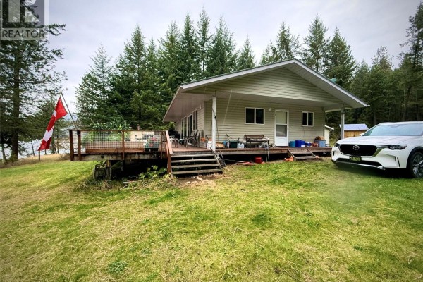 Exterior of a light-colored house with a covered deck and a vehicle parked nearby. - 7180 Little Cayuse Creek Road, Castlegar
