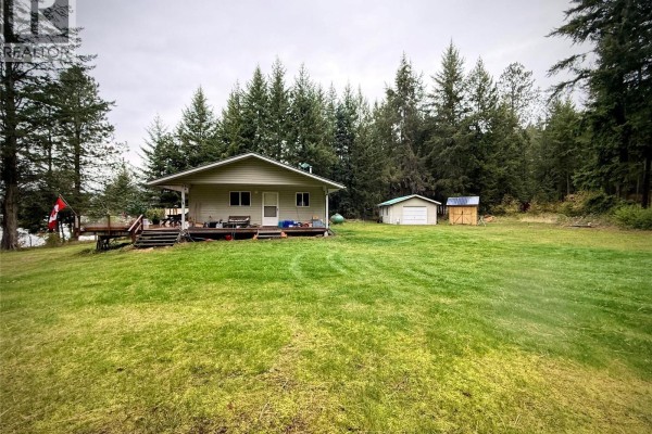 View of the house and surrounding grassy area with evergreen forest behind. - 7180 Little Cayuse Creek Road, Castlegar