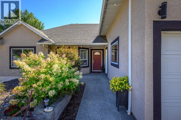Pathway leading to the front entrance of the house, with landscaping and shrubs. - 7185 Old Kamloops Road, Vernon