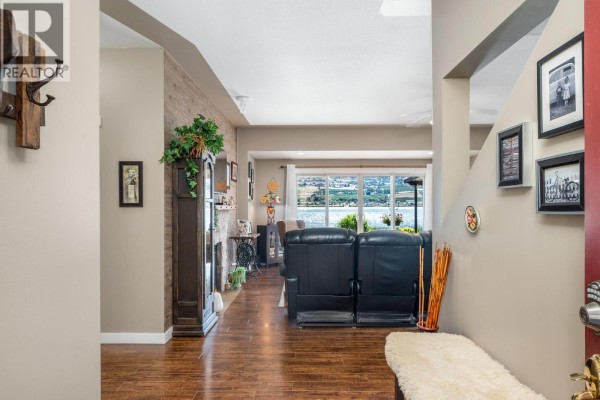 Interior view of the living area, showing leather recliners, a brick fireplace, and a view of the lake. - 7185 Old Kamloops Road, Vernon