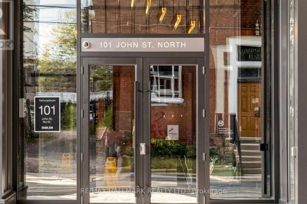 Close-up of a building entrance with glass double doors, signage, and reflective windows. - 719 - 101 John Street N, Hamilton