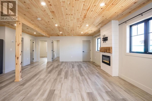Living room interior featuring a fireplace, multiple doorways, light grey flooring, and a wood-paneled ceiling. - 71b Woodleigh Drive, Kensington