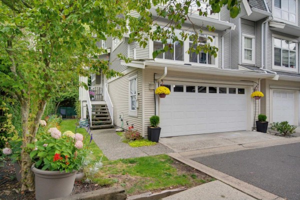 Front exterior of a grey townhouse with a white garage door and landscaping. - 72 6450 199 Street, Langley