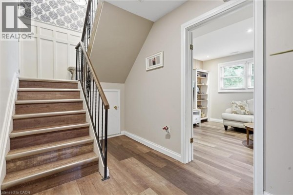 Hallway with wood-look flooring, ornate banister, and doorway to living area with sofa - 72 Crestlynn Crescent Simcoe