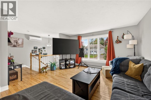 Living room with a sectional sofa, large TV, hardwood floors, and a large window. - 72 Devarenne Street, Dieppe