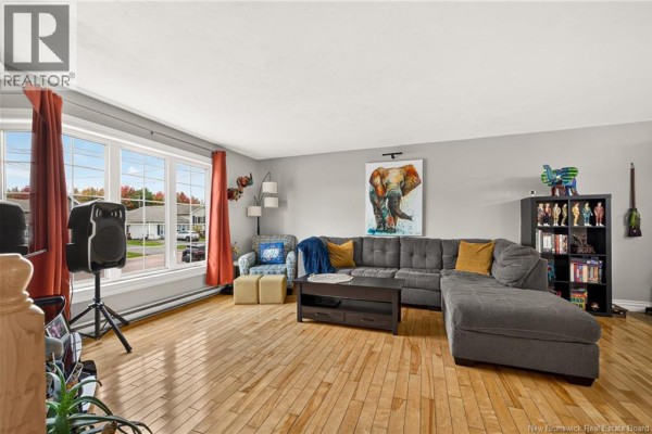 Living room featuring a grey sectional sofa, hardwood floors, and a large window with a view of the street. - 72 Devarenne Street, Dieppe