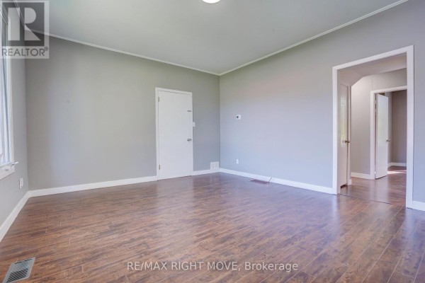 Empty room with grey walls, wood-look laminate flooring, and doors to other rooms. - 72 Dunedin Street, Orillia