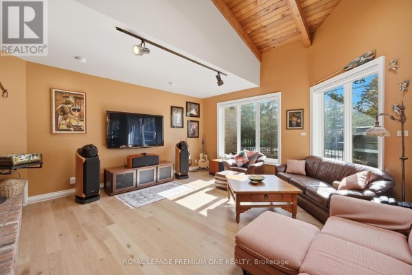 Living room with vaulted wood-beamed ceiling, leather sofa, large television, and hardwood floors. - 72 Golf Avenue, Vaughan
