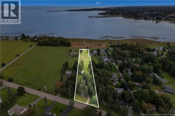 Aerial view of a rural property with a white outline, showing the house, treed lot, and proximity to water. - 72 Hanington, Shediac Cape