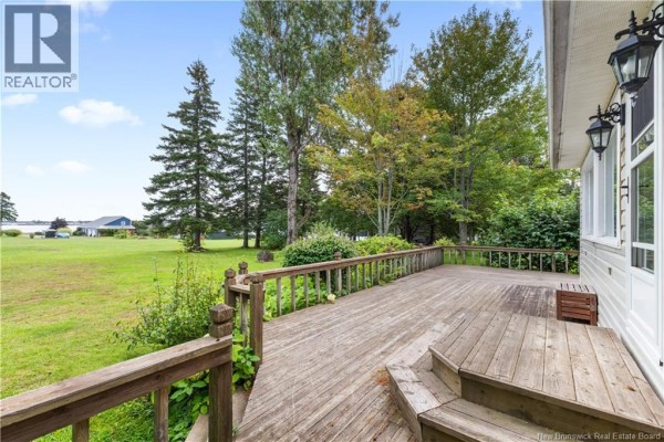 Wooden deck with railing and steps, overlooking a large green lawn and distant water views under a blue sky. - 72 Hanington, Shediac Cape