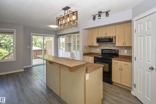 Kitchen with light wood cabinets, black appliances, a granite countertop island, and dark wood flooring. - 72 Hartwick Ld, Spruce Grove