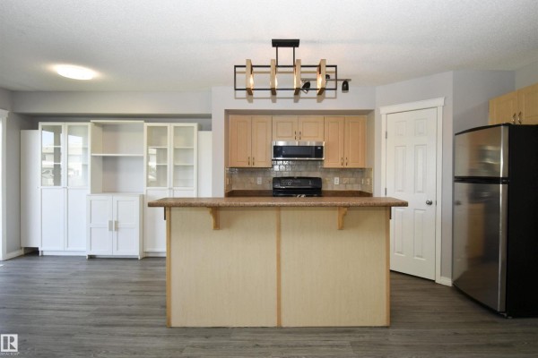 Kitchen with light wood cabinets, stainless steel refrigerator, island, and dark wood flooring. - 72 Hartwick Ld, Spruce Grove
