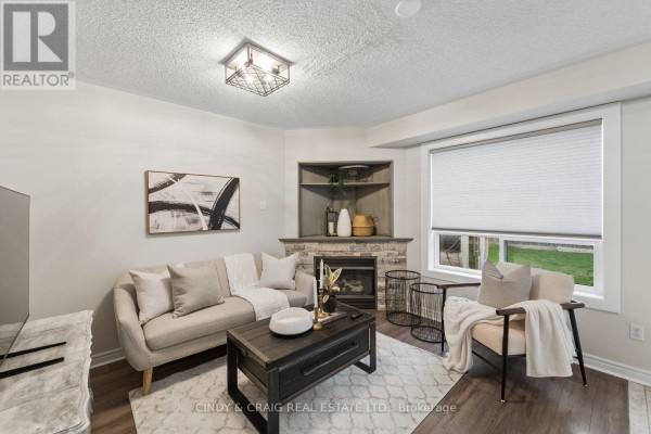 Living room with a sofa, armchair, coffee table, and a stone fireplace surround. - 72 Lafayette Boulevard, Whitby