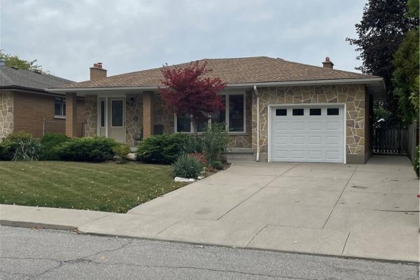 View of the house from the driveway, showing a stone facade, white garage door, and concrete driveway. - 72 Purnell Drive, Hamilton