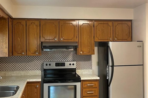 Kitchen area with stainless steel refrigerator, black range, oak cabinets, and tiled backsplash. - 72 Purnell Drive, Hamilton