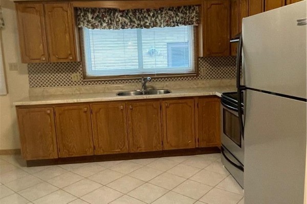Kitchen view showing a double sink under a window, oak cabinets, and a stainless steel refrigerator. - 72 Purnell Drive, Hamilton