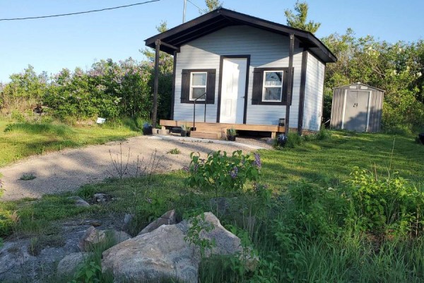 Small grey building with black trim and two windows, viewed from a gravel driveway with rocks and grass. - 72 Store Street, Tweed)