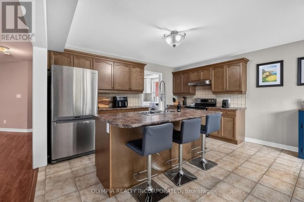 Kitchen with dark wood cabinets, island with bar stools, stainless steel refrigerator, and tile flooring. - 72 Tuliptree Road, Thorold