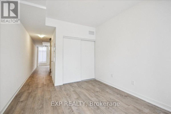 Bedroom with white walls, white sliding closet doors, and grey wood-look flooring. - 72 Turtle Island Road, Toronto