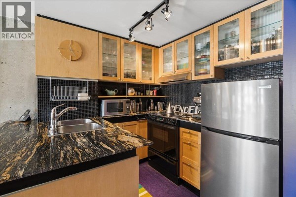 Small galley kitchen with wood cabinets, granite countertops, stainless steel appliances, and black tile backsplash. - 720 1333 Hornby Street, Vancouver
