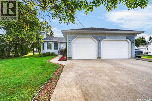 Front exterior of a house with a grey stucco finish and a double garage door. - 720 6th Avenue, Rosthern