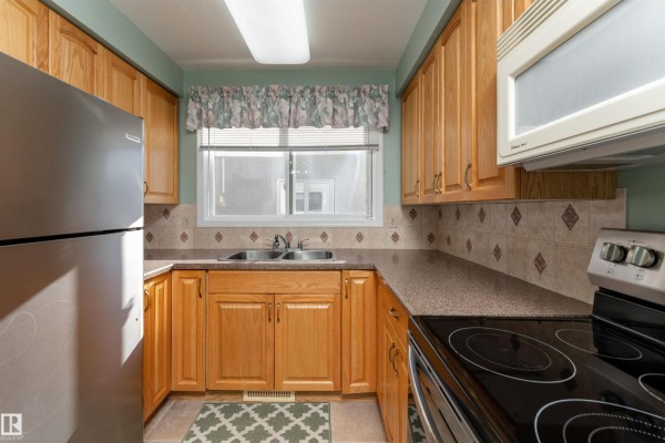 Kitchen with light wood cabinets, speckled countertops, stainless steel refrigerator, and beige tiled floor. - 720 Knottwood Rd S Nw, Edmonton