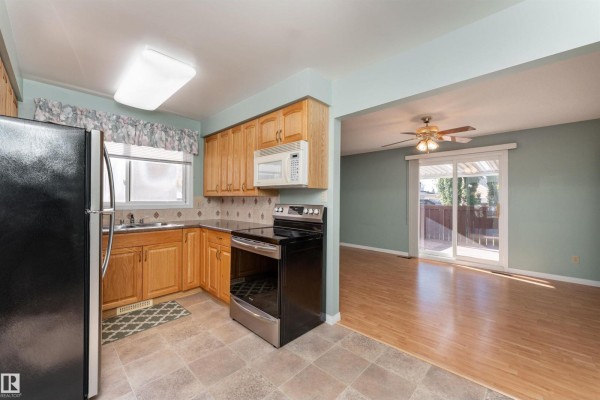 Kitchen area opening to a living space with wood laminate flooring and a sliding glass door. - 720 Knottwood Rd S Nw, Edmonton