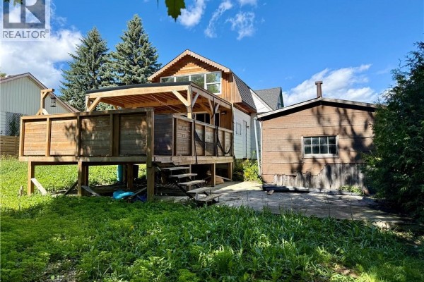 Backyard view with a large wooden deck, detached wooden shed, and green lawn under a blue sky. - 720 Main Street W, Listowel