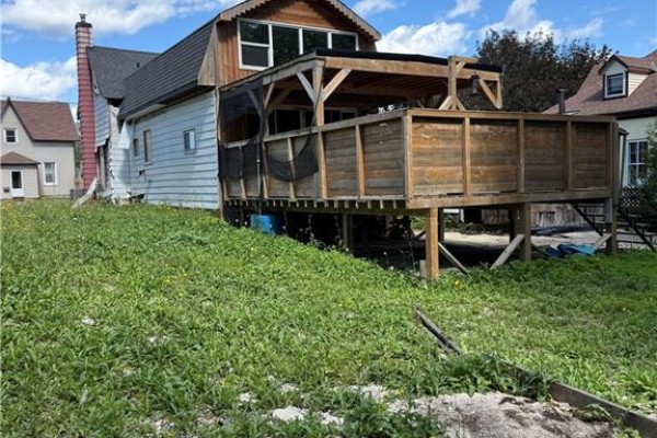 Side and back view of a house with a wooden deck and overgrown grass, showing a shed and neighboring properties. - 720 Main Street W, Listowel