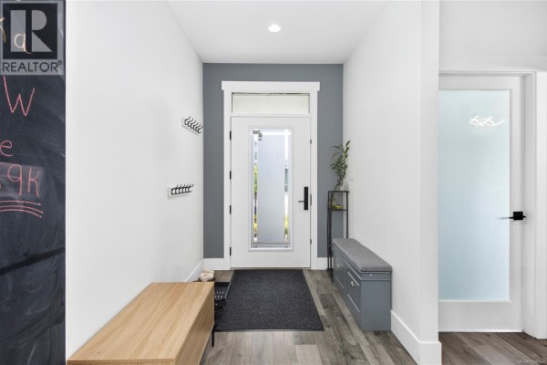 Interior foyer with a wooden bench, coat hooks, and a frosted glass front door. - 720 Sitka St, Campbell River
