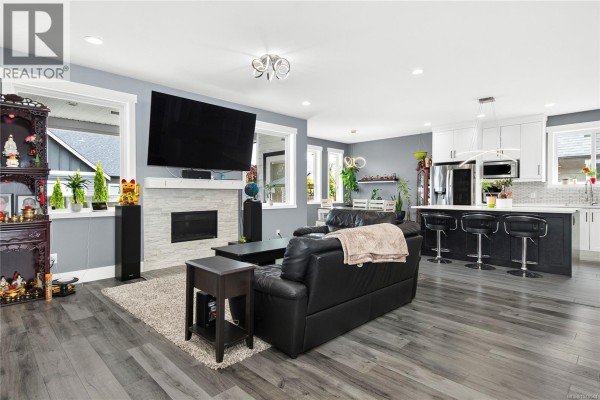 Living room and kitchen with a fireplace, black leather sofa, and a breakfast bar with stools. - 720 Sitka St, Campbell River