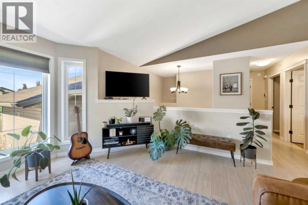 Living room with a television, media console, plants, and an entryway beyond. - 7207 39a Street, Lloydminster