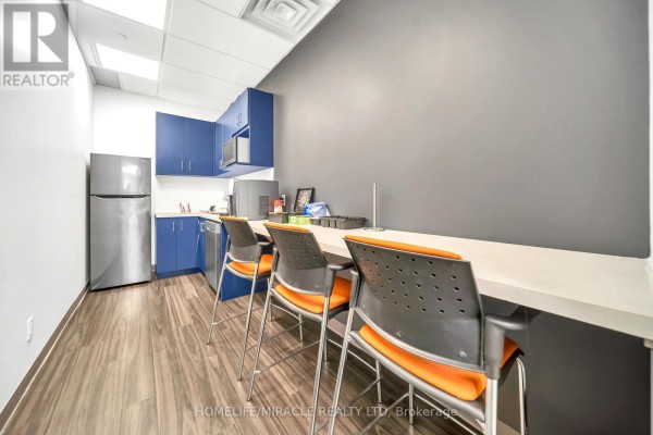 Office kitchen area with blue cabinets, stainless steel appliances, and a long counter with chairs. - 721 - 130 Queens Quay E, Toronto