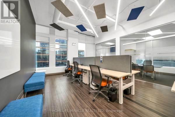 Open office space with desks, chairs, blue benches, and glass-walled offices. - 721 - 130 Queens Quay E, Toronto