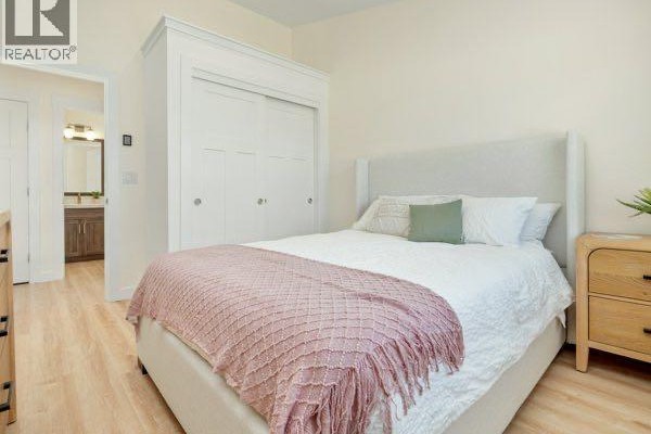 Bedroom with a bed, white closet doors, a nightstand, and a view of a bathroom. - 721 7 Avenue W, Cardston