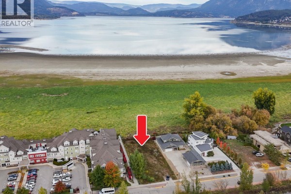 Aerial view of a vacant lot marked with a red arrow, surrounded by apartment buildings and houses, near a large lake. - 721 Harbourfront Drive, Salmon Arm