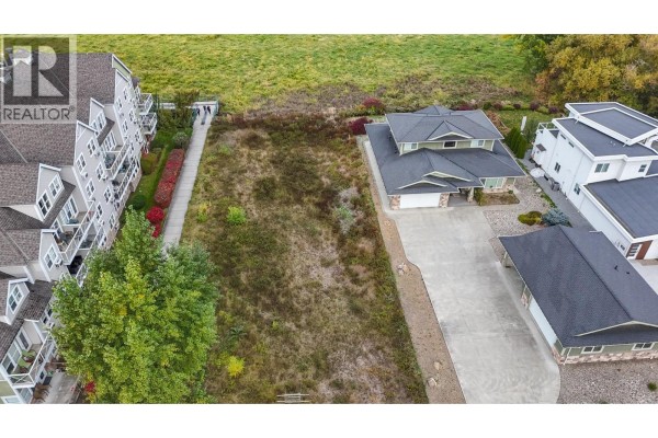 Aerial view of a vacant lot between two houses, showing adjacent apartment buildings, driveway, and surrounding vegetation. - 721 Harbourfront Drive, Salmon Arm