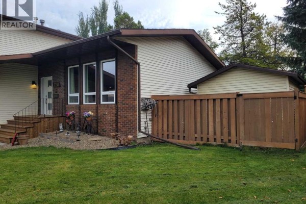 Side view of the house showing beige siding, brick, and a wooden privacy fence. - 7214 97 Street, Grande Prairie