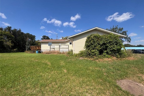 Back exterior of a cream-colored house with tan siding and a large overgrown bush near the corner. - 72140 96 Rd N Road N, Plumas