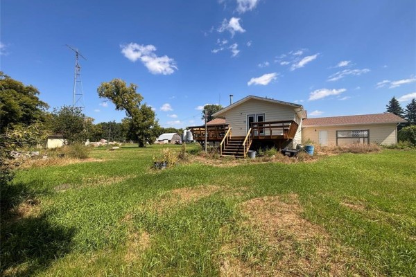 Distant view of a cream-colored house with a wooden deck and scattered trees under a blue sky. - 72140 96 Rd N Road N, Plumas
