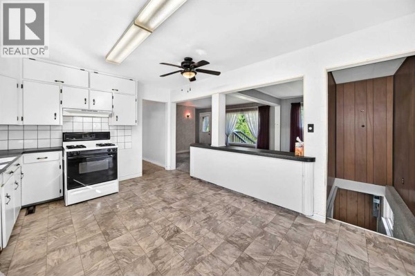 Kitchen with white cabinets, black countertops, tiled floor, and an opening to the living area. - 7219 Bow Crescent Nw, Calgary