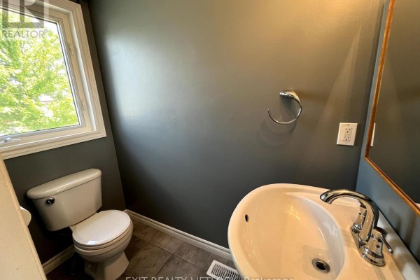 Powder room with a toilet, sink, and a window overlooking green trees. - 722 Trailview Drive, Peterborough