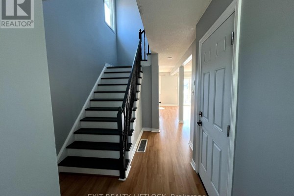 Entranceway with hardwood floors, a staircase with black treads, and a gray door. - 722 Trailview Drive, Peterborough